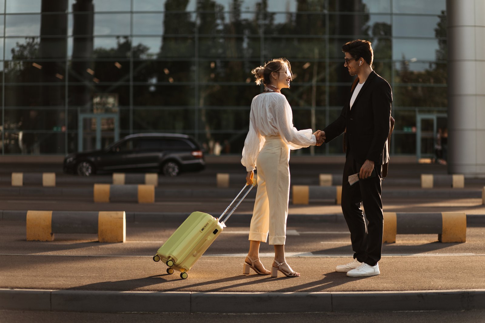 Woman with a lime green suitcase greeting a man outside of an office building | On The Road Again | Acro Commerce